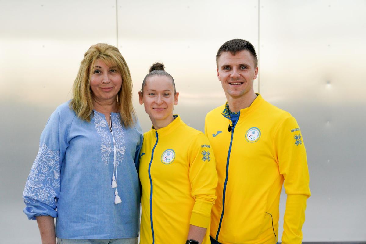 Oksana Kozyna and Oleksandr Chyrkov standing with their teacher and smiling